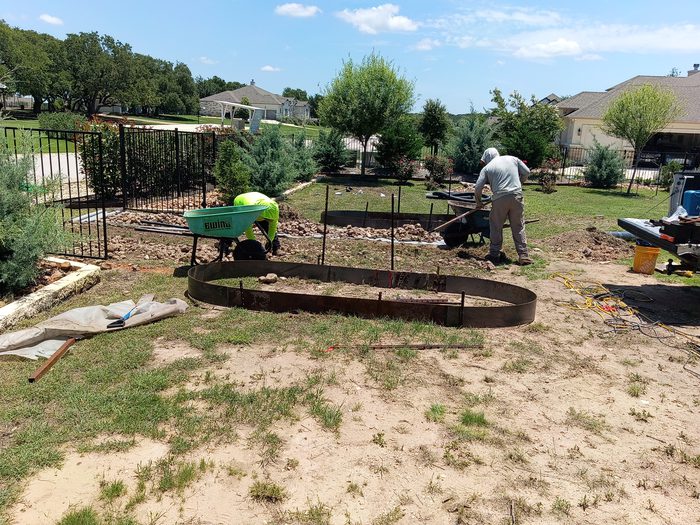 The Cardenas Landscaping crew installing steel bed edging and moving soil in a Central Texas backyard